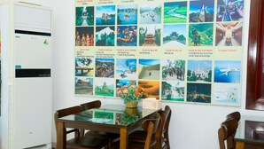 A dining area with a glass table and wooden chairs, a white air conditioner, and a wall with a collage of travel photos. - Luxury Airport Hotel & Travel (Hanoi)