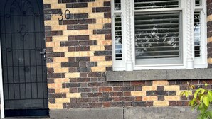 Fachada de tijolos com uma porta numerada, uma janela com persianas e uma pequena planta.