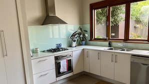 Cozinha moderna com armários brancos, fogão a gás, forno, lava-louças e janela com vista para o verde lá fora.