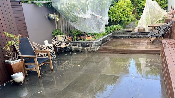 Um pátio com piso de azulejos, mobiliário para áreas externas, plantas em vasos e um espaço coberto para sentar.