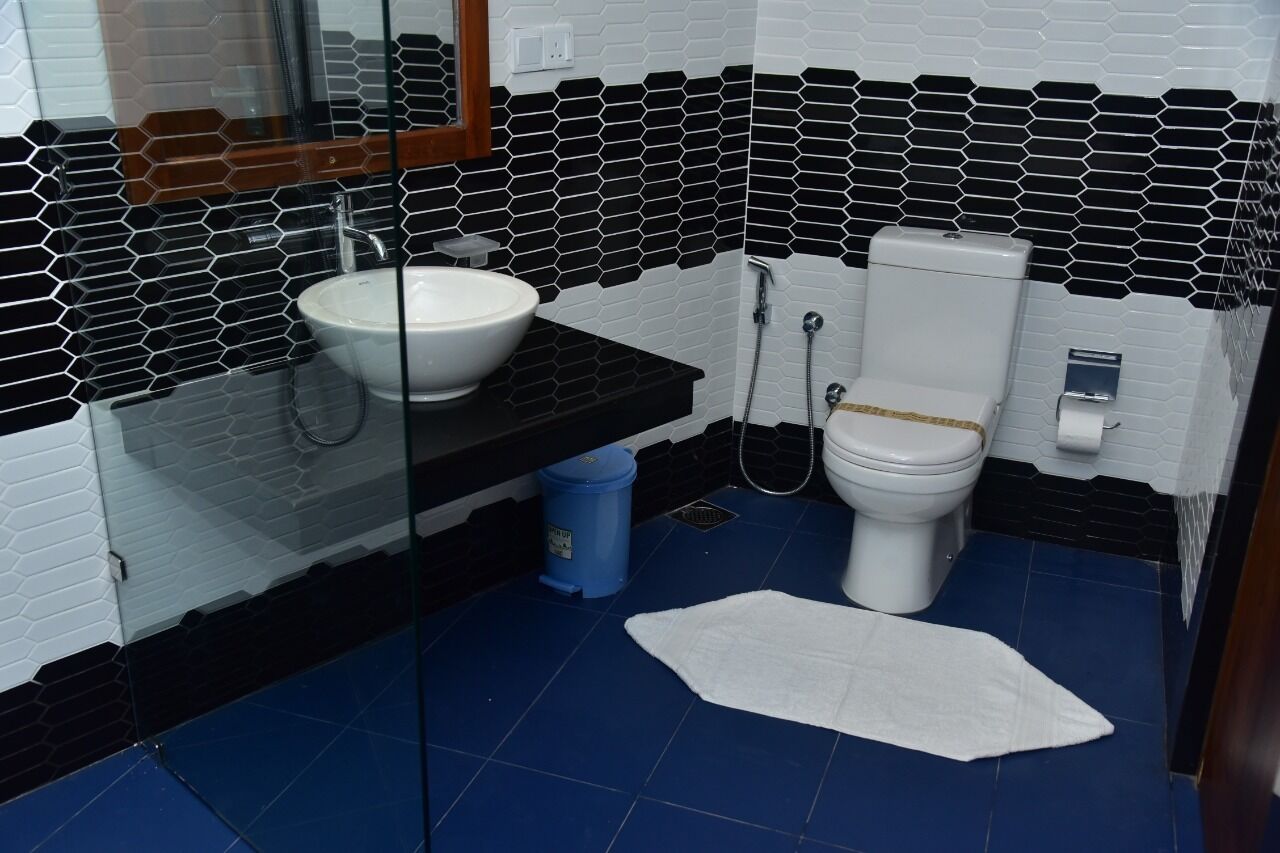 Un baño con un lavabo blanco, paredes con azulejos blancos y negros, suelo azul y una toalla blanca en el suelo.
