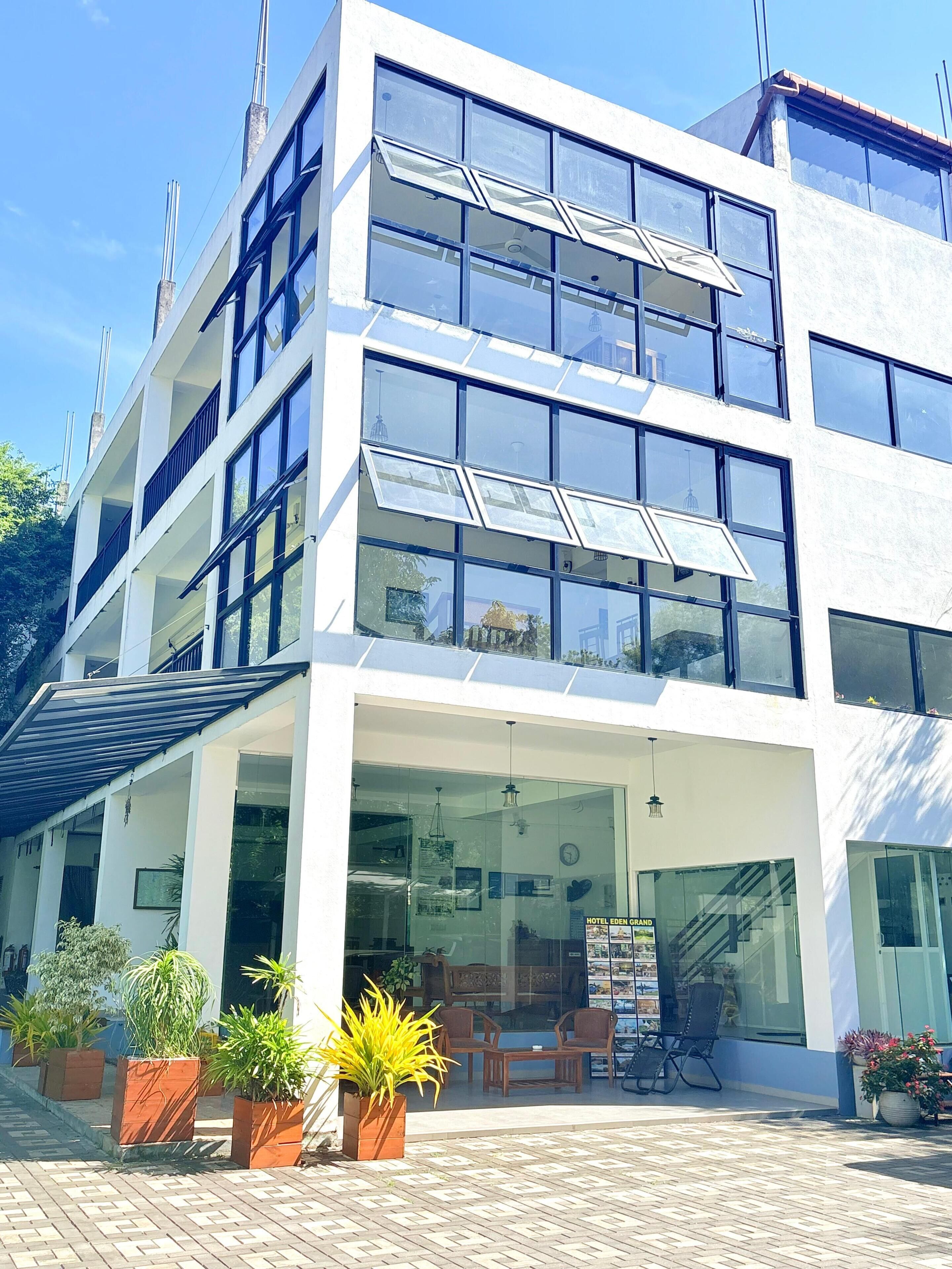 A modern hotel with multiple floors, large windows, and a covered outdoor seating area with potted plants.