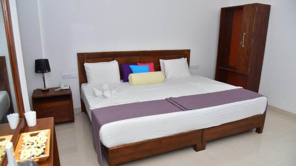 A neatly arranged hotel room with a large bed, a wooden wardrobe, a nightstand with a lamp, and a small table with a tray of flowers.
