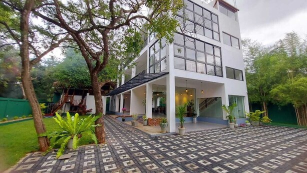A modern two-story building with large windows and a covered outdoor area with potted plants. - Eden Grand (Dambulla)