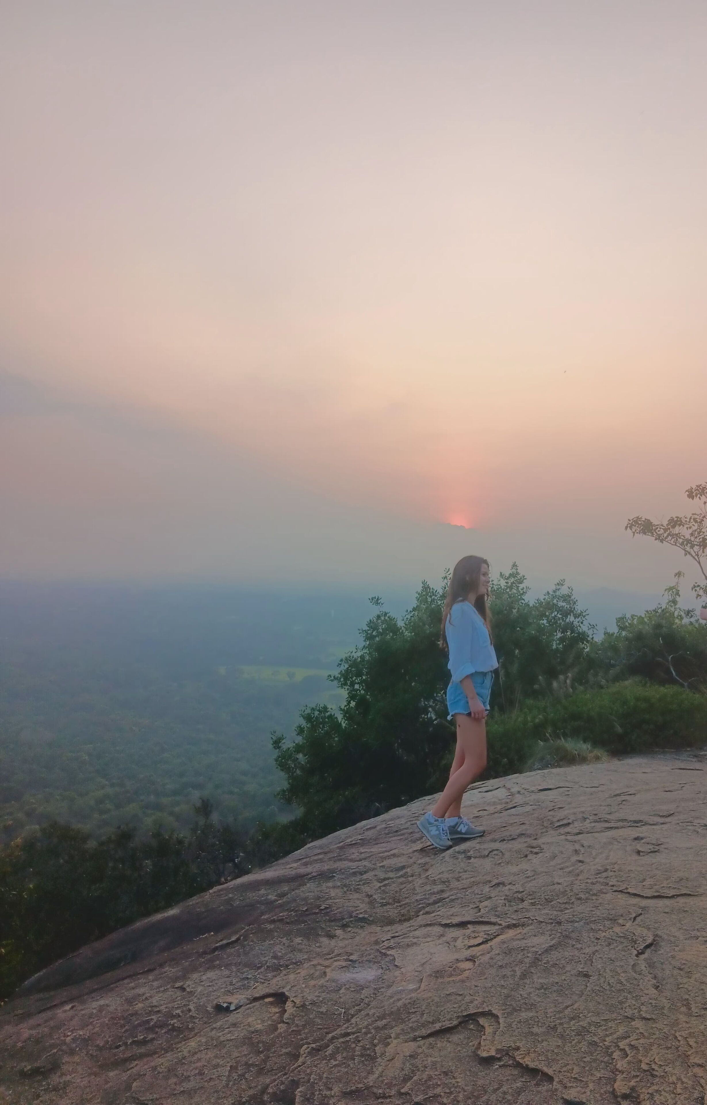 A person standing on a rocky outcrop overlooking a valley.