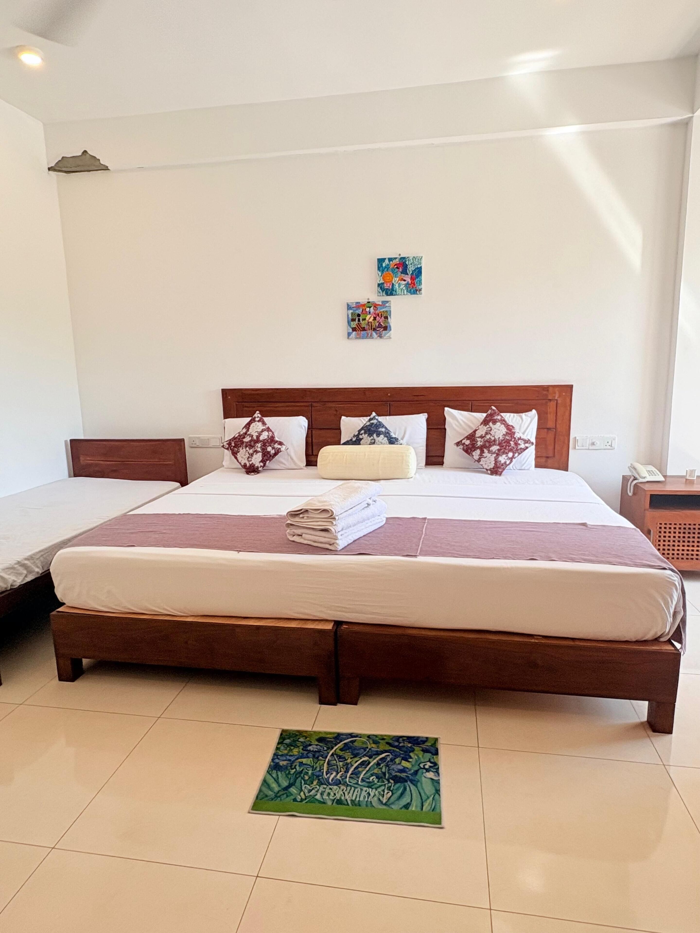 Habitación de hotel con una cama grande, dos mesitas de noche, una mesita auxiliar pequeña, un teléfono montado en la pared y un felpudo decorativo.