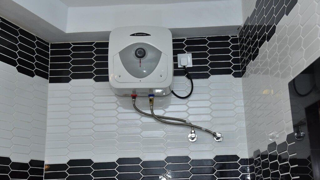 A bathroom with a white and black hexagonal tile pattern, a white water heater, and a metal faucet.