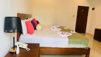 A neatly arranged hotel room with a bed, a bedside table with a lamp and phone, and a door in the background.