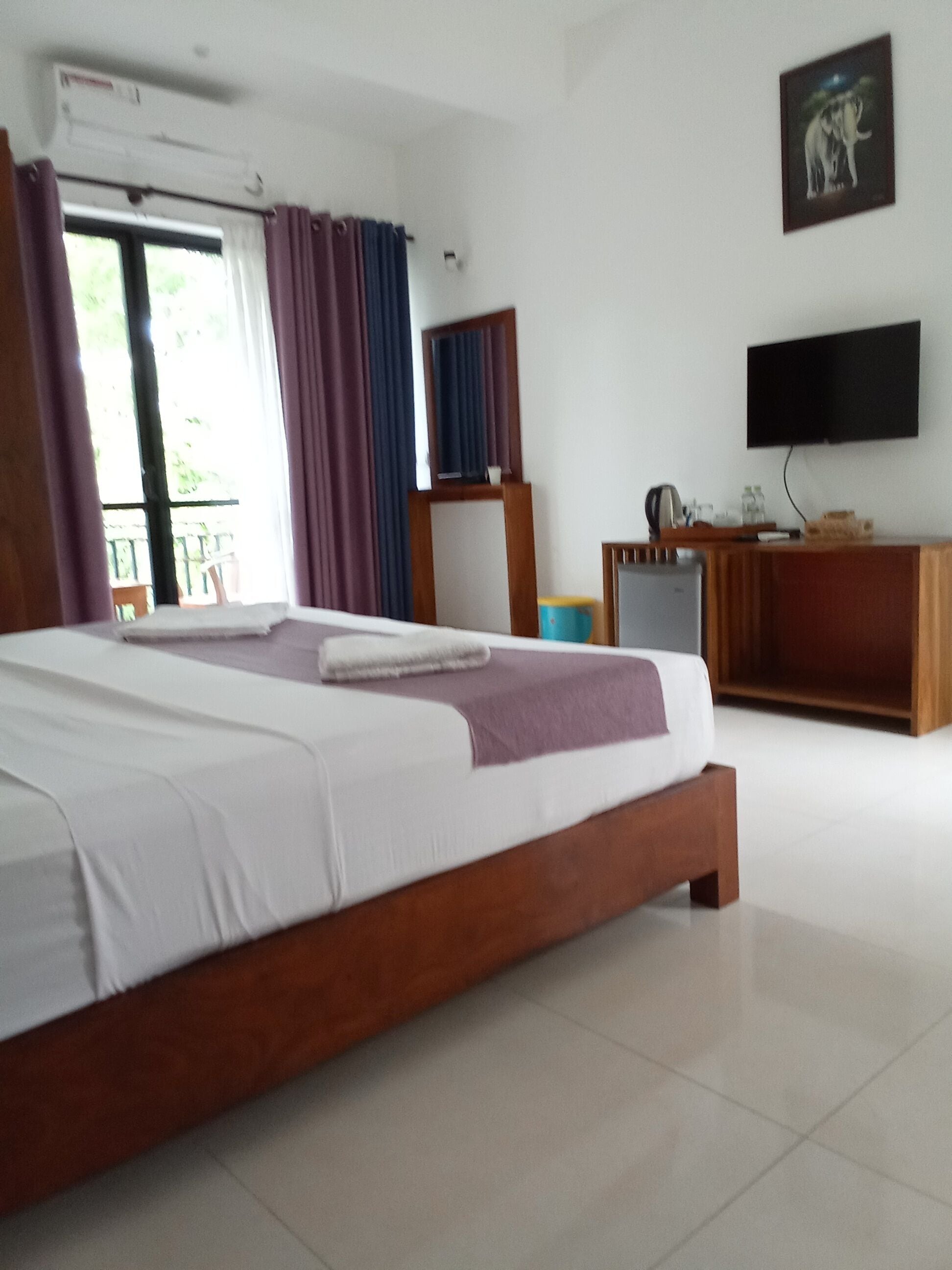 A hotel room with a large bed, a television, a desk, and a window with curtains.