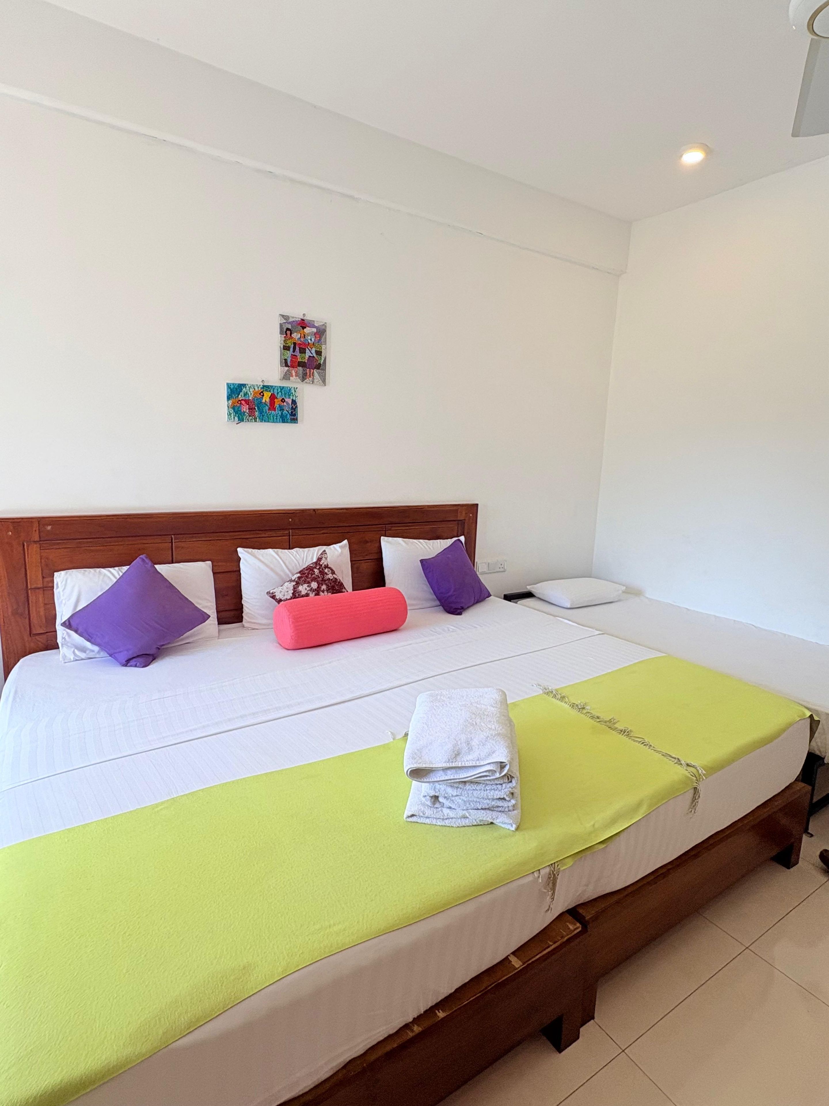 A single bed with a wooden headboard, white bedding, and a green blanket.