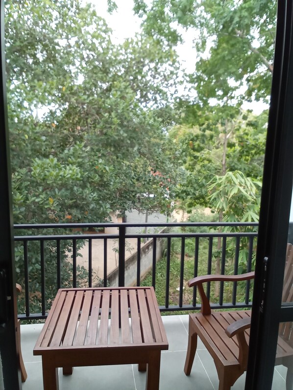 Un balcon agrémenté de deux tables et de chaises en bois, entouré d’une rambarde en métal noir.