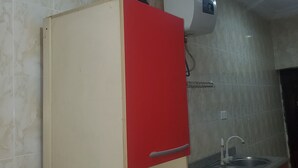 A kitchen with a red and beige cabinet, a white air conditioner, and a stainless steel sink. - Miraph Apartment (Abuja)
