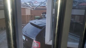 A view through a window with a metal frame, featuring a black car parked outside. - Miraph Apartment (Abuja)