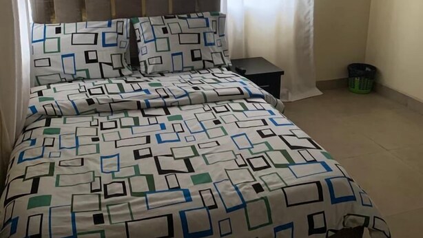 A bedroom with a bed, a nightstand, a wall-mounted air conditioner, and a window with curtains. - Miraph Apartment (Abuja)