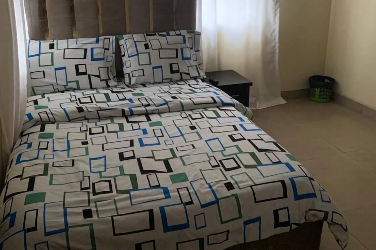 Un dormitorio con cama, mesita de noche, aire acondicionado instalado en la pared y ventana con cortinas.