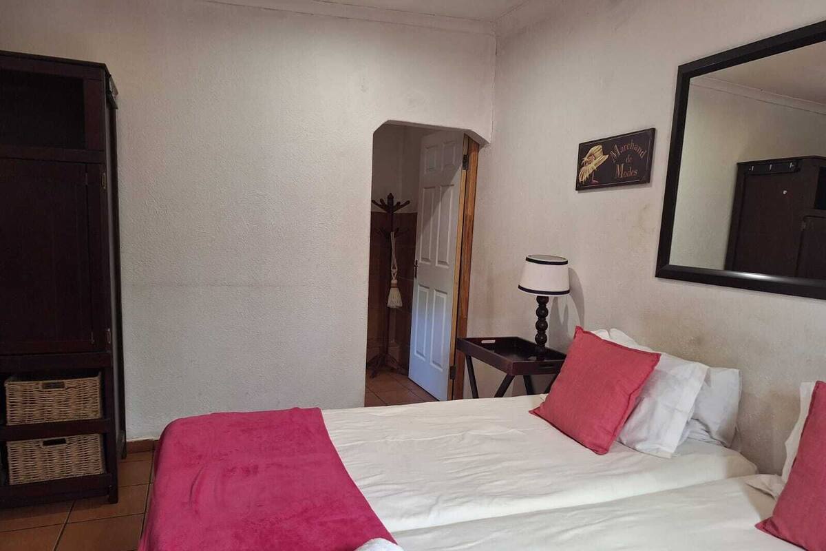 Quarto de hotel com cama, mesa de cabeceira, abajur, guarda-roupa e espelho.