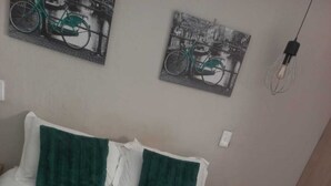 En snyggt bäddad säng med vita och mörkgrå sängkläder, två gröna kuddar och två hoprullade vita handdukar på sängen.