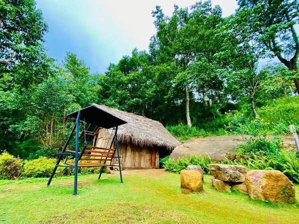 A rustic hut with a thatched roof, surrounded by lush greenery and a wooden bench. - Hanthana Eco Lodge (Puliyadda)