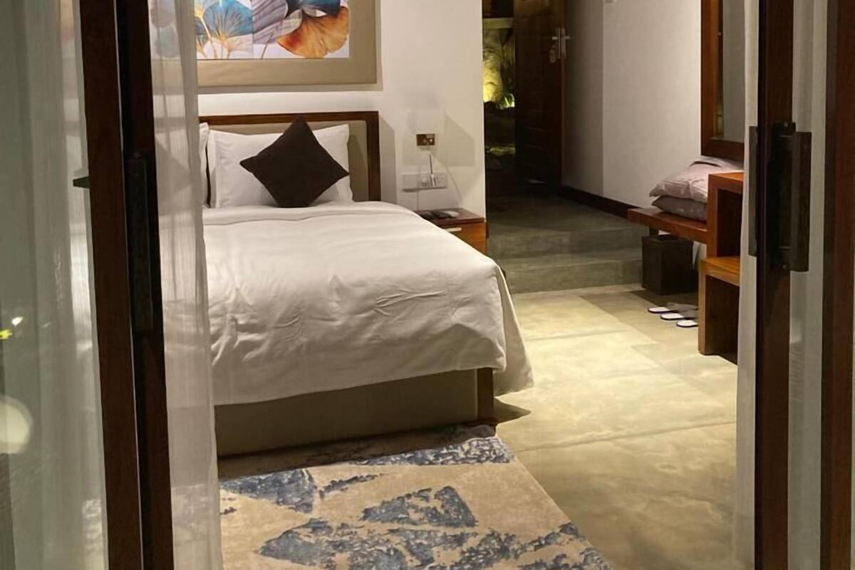 A bedroom with a bed, a ceiling fan, a painting, and a view into another room.