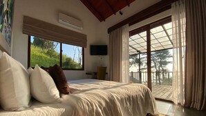 Ein Schlafzimmer mit einem großen Bett, einem Fernseher und einem Balkon mit Blick auf Bäume.