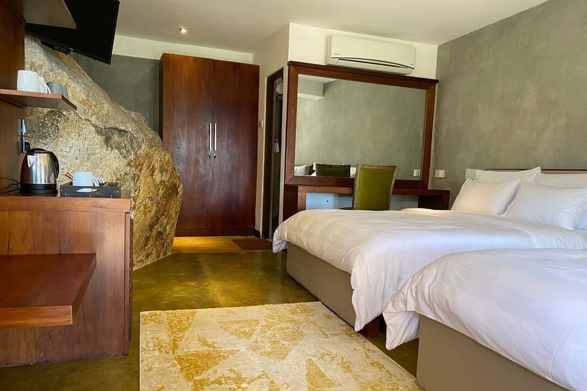 A bedroom with a bed, a desk, a chair, a mirror, and a large rock feature.