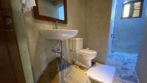 Ein Badezimmer mit einem SteinklopfZuber, einer weißen Toilette und einer Duschkabine mit Steinböden.