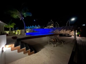 A nighttime outdoor area with a swimming pool, steps leading to a deck, and outdoor seating.