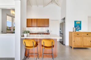 A modern kitchen with wooden cabinets, a white countertop, and two yellow bar stools.