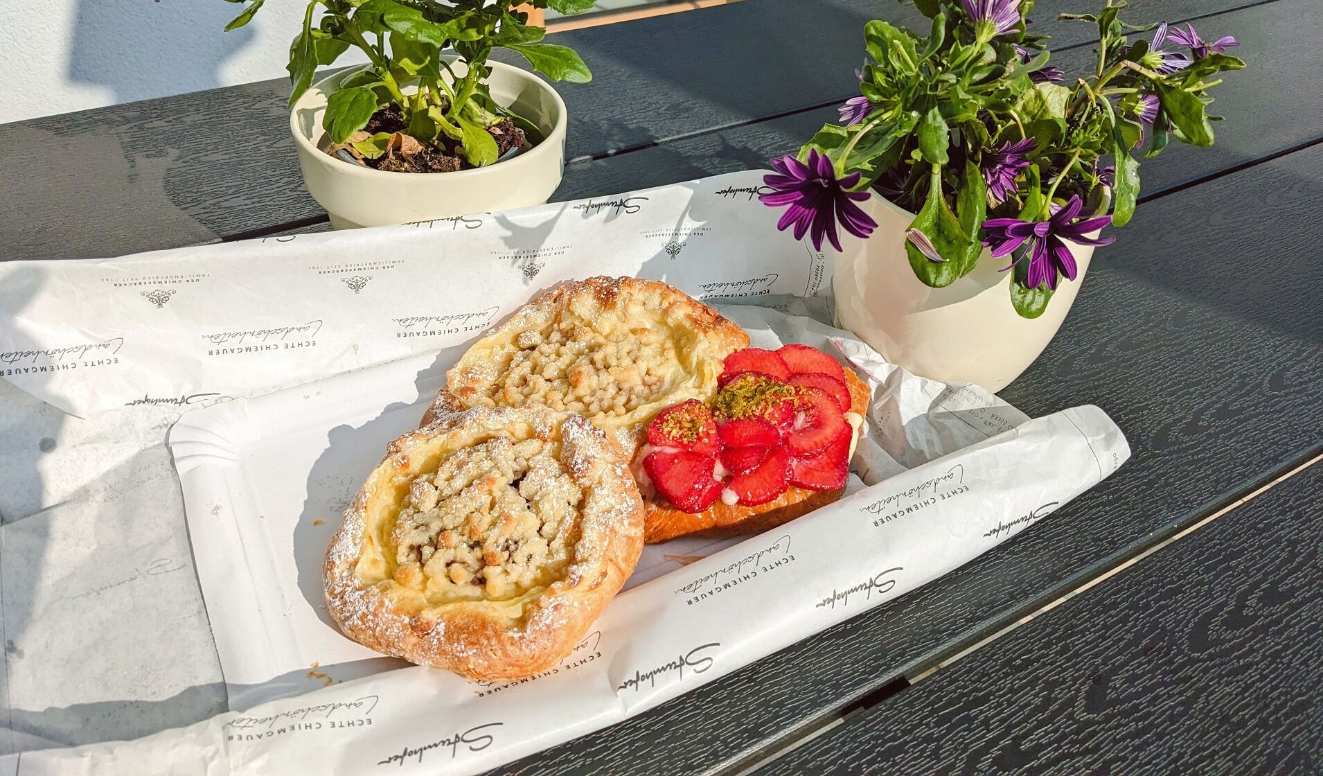 A tray with two pastries and a strawberry slice on a table with two potted plants.