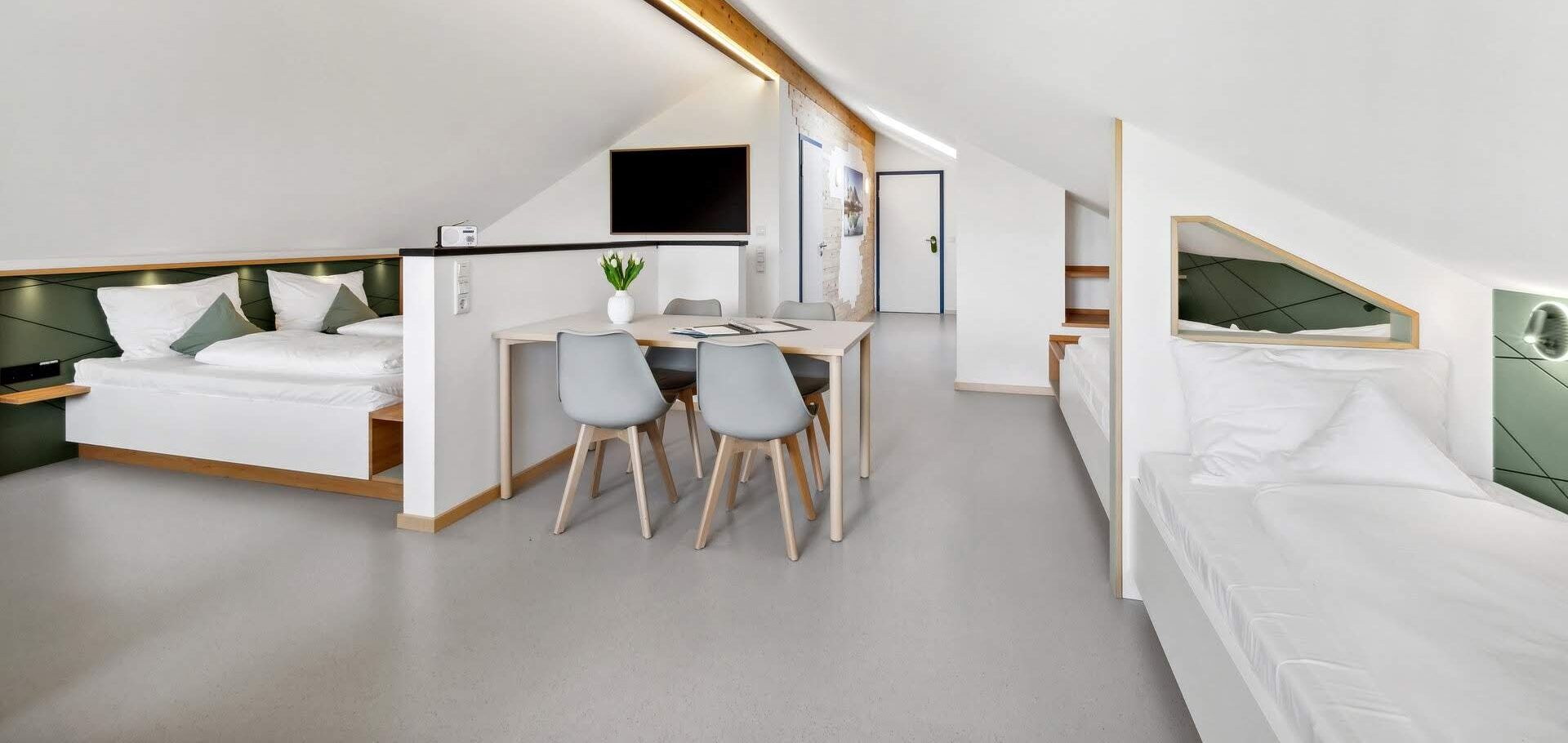 Een moderne, compacte kamer met een bed in loftstijl, een bureau en twee stoelen.