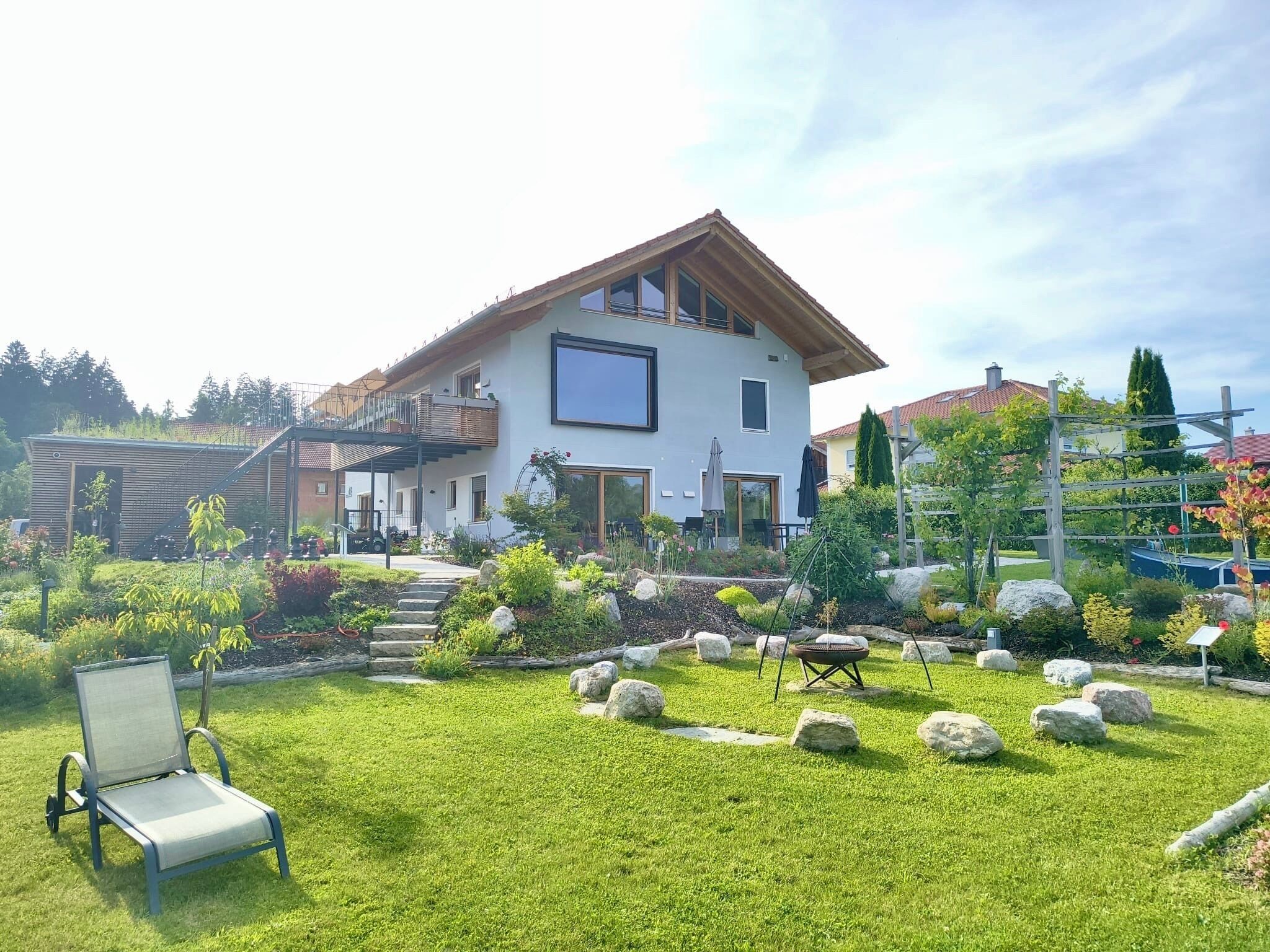 A modern two-story house with a spacious garden, a patio with outdoor furniture, and a clear view of the surrounding area.