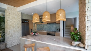 Una cocina moderna con una isla grande, taburetes de bar de madera y lámparas colgantes de mimbre.