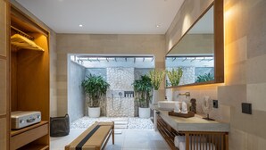 Un baño moderno con ducha de piedra, banco de madera y un espejo grande.