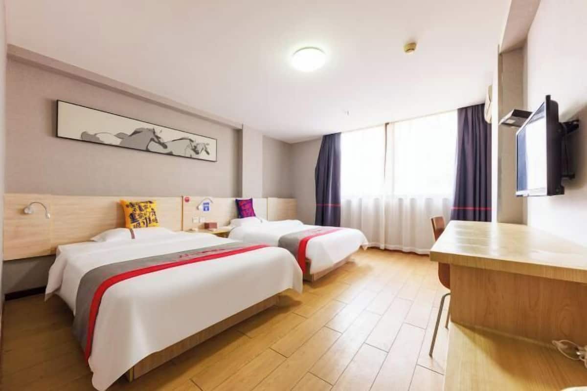 Habitación de hotel con dos camas, un escritorio, un televisor y una ventana con cortinas.
