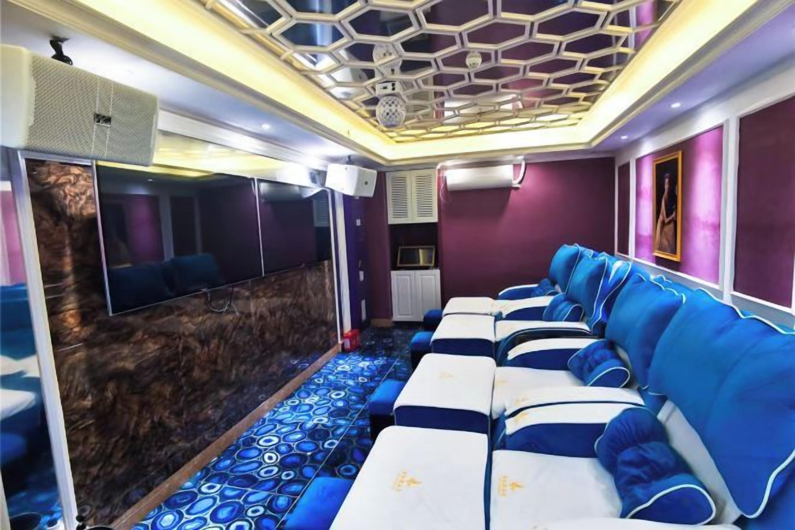 A room with a row of beds, a wall-mounted TV, and a patterned carpet.