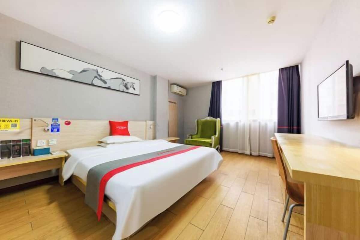 Habitación de hotel con cama, escritorio, silla, televisión y ventana con cortinas.