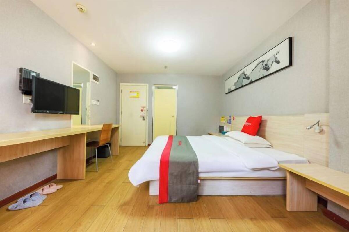 Habitación de hotel con cama, escritorio, televisor, silla y puerta.