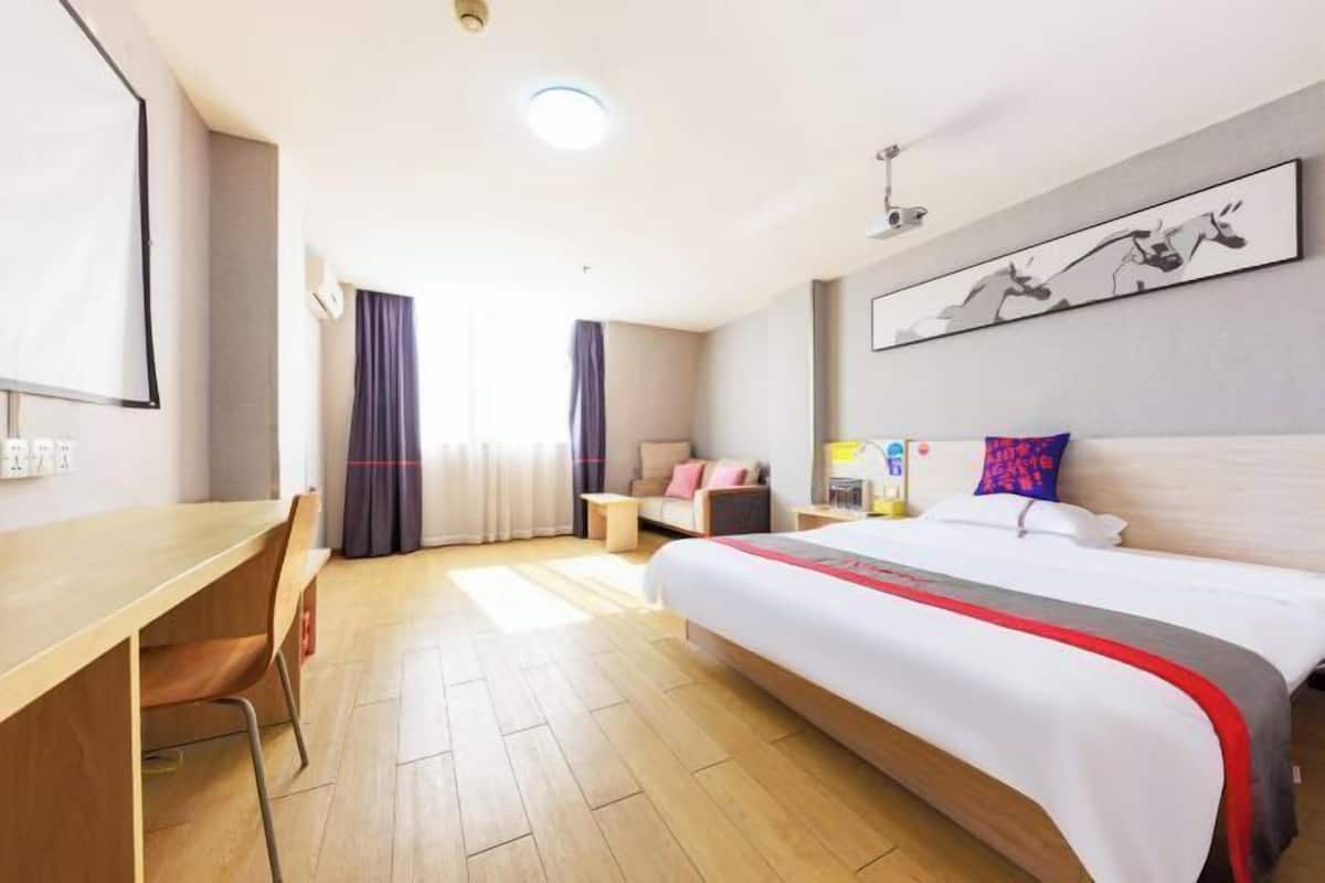 Una habitación de hotel con cama, escritorio, silla, sofá, mesa de centro y un cuadro en la pared.