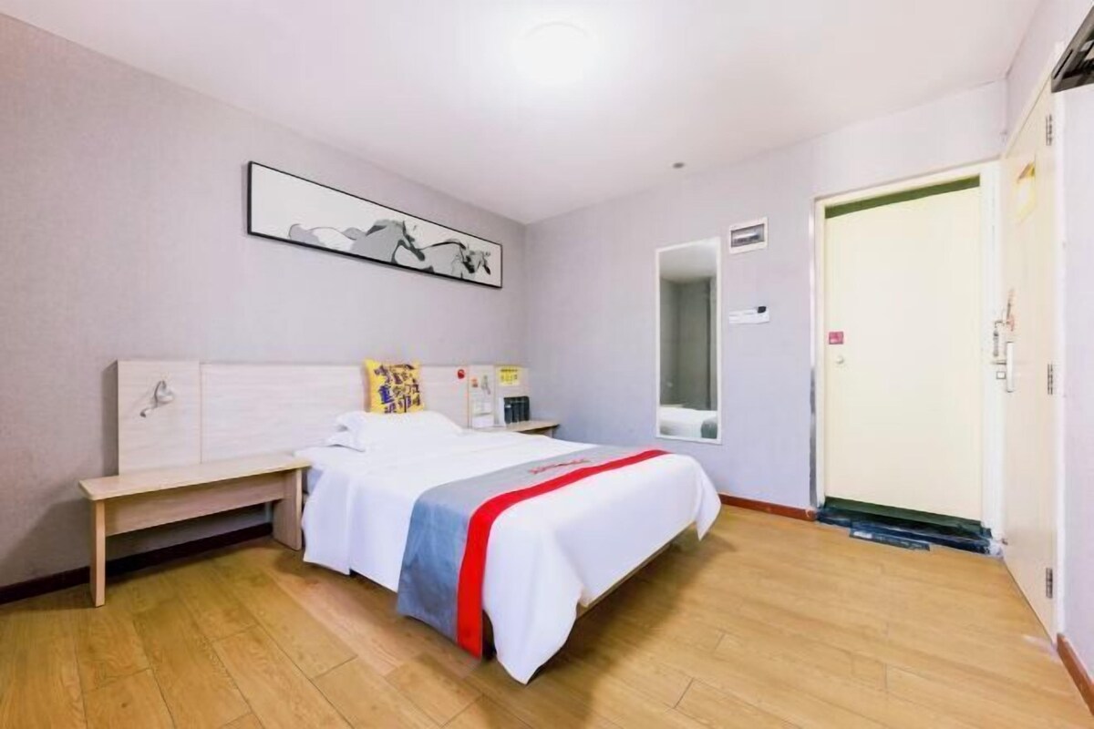 A hotel room with a bed, bedside table, a mirror, a wardrobe, and a framed picture on the wall.