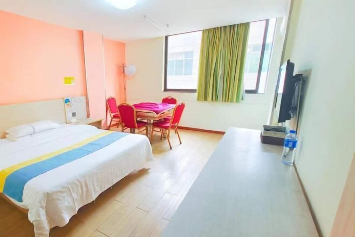 Habitación de hotel con cama, escritorio, silla, mesa, televisor y ventana con cortinas.