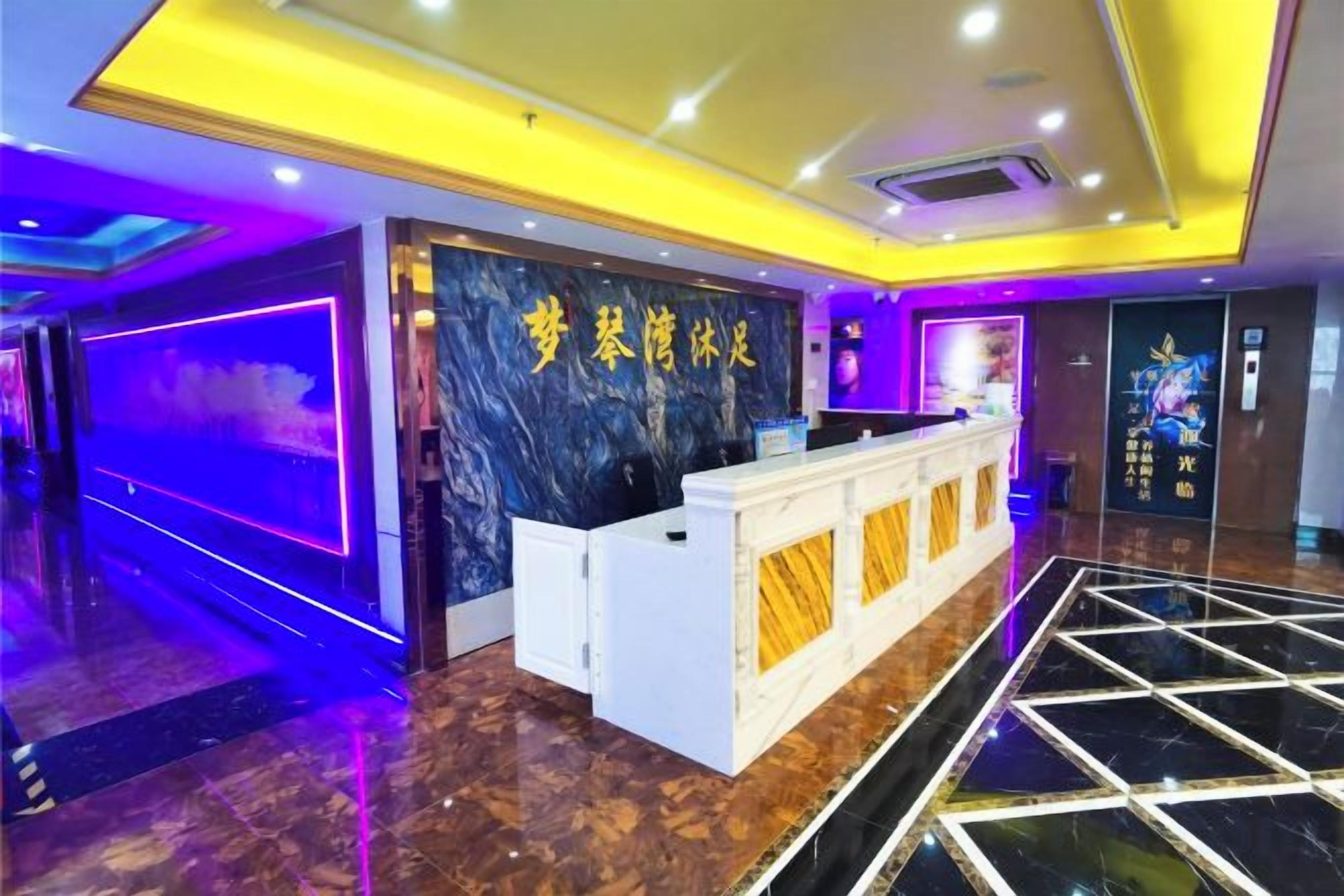 A hotel reception area with a marble reception desk, a purple-lit wall, and a tiled floor.