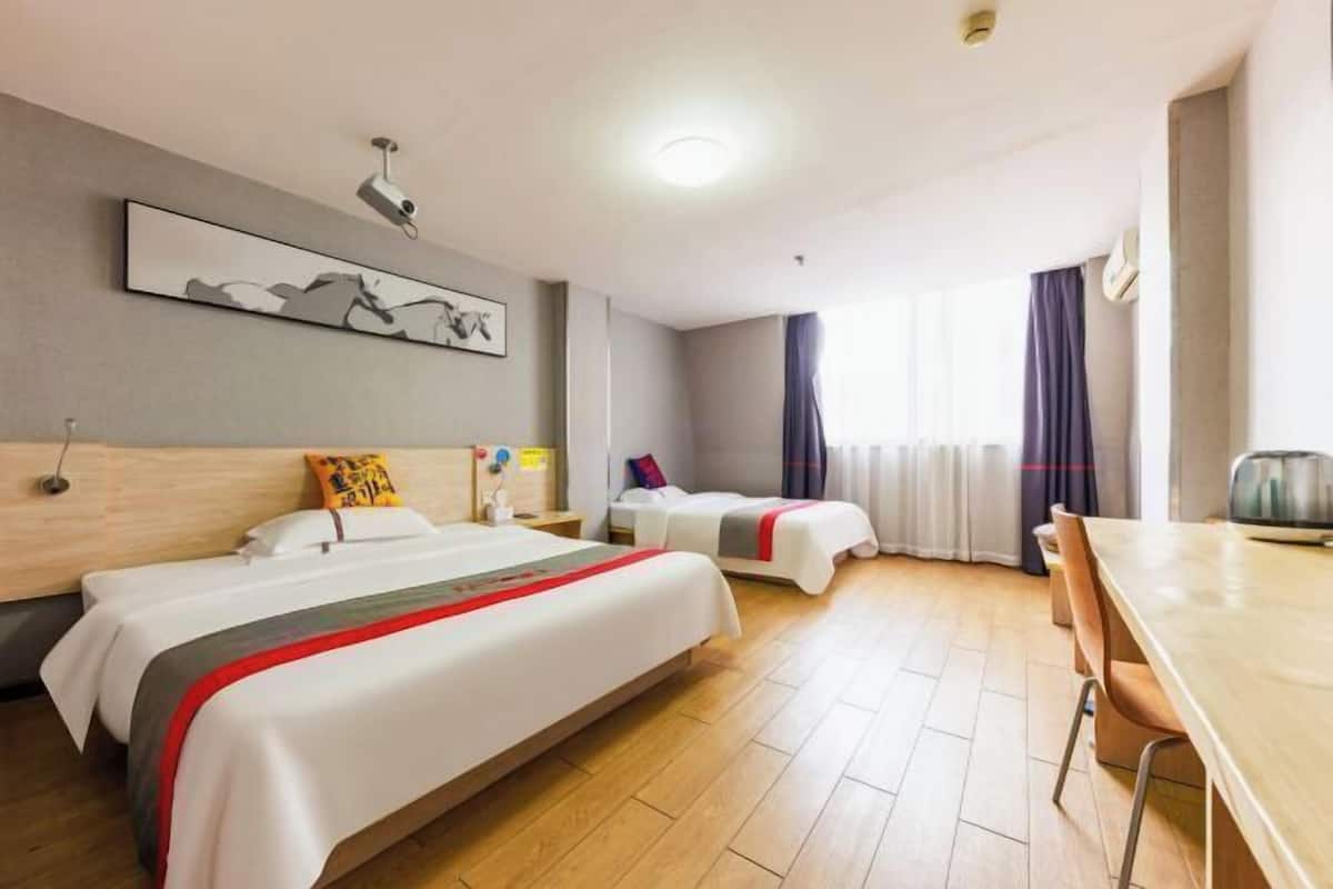 Habitación de hotel con dos camas, una mesa de comedor, un proyector y un ventanal con cortinas.