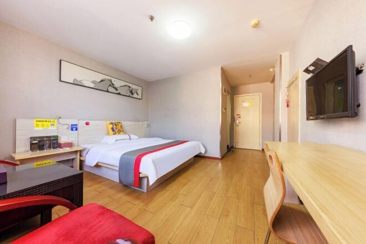 A hotel room with a bed, a desk, a chair, a TV, and a door leading to another room.