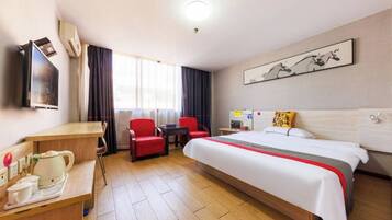 Habitación de hotel con cama, escritorio con hervidor, dos sillas rojas, televisión y ventana con cortinas.