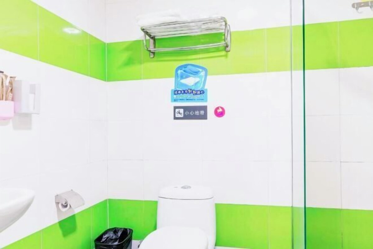 A bathroom with green and white tiles, a white sink, a toilet, and a trash bin.