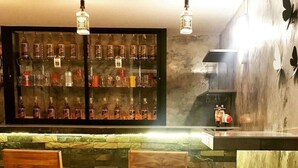 A bar area with two wooden bar stools, a shelf with various bottles, and a brick wall. - Baan Bua Talay (Rayong)