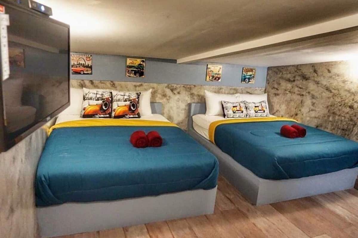 Ein Zimmer mit zwei Betten, jeweils mit blauer Bettdecke und Kissen mit Zeichentrickfiguren. An der Wand über den Betten ist ein Flachbildfernseher angebracht.