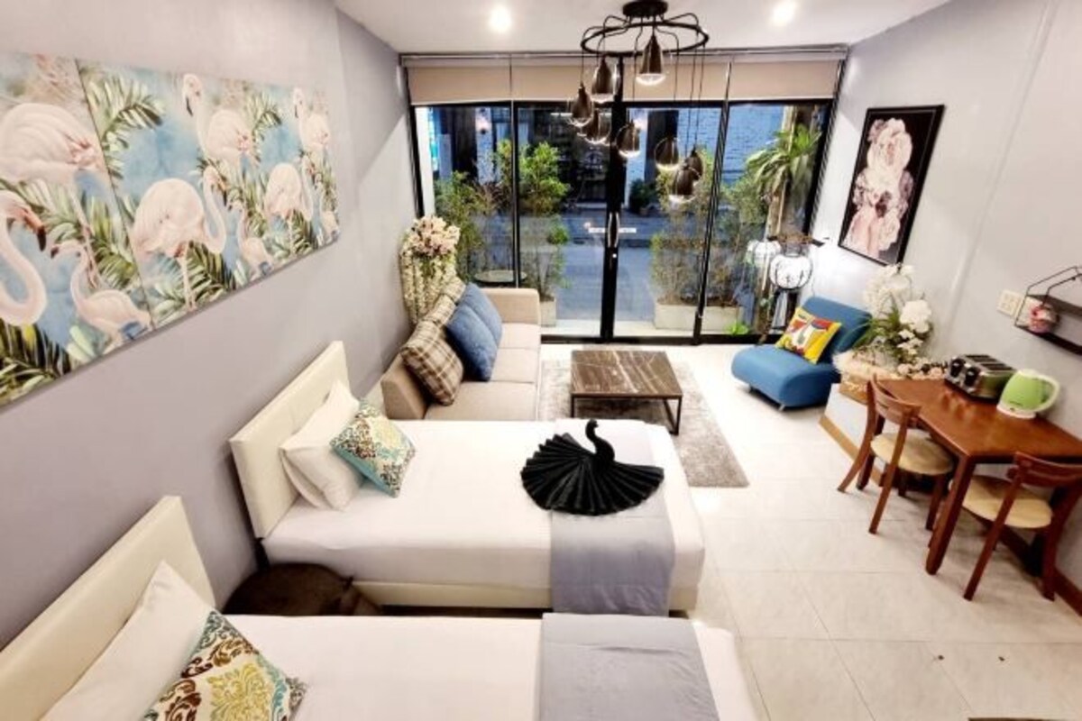 A modern living room with a sofa, a dining table, and a large window with a view of greenery.
