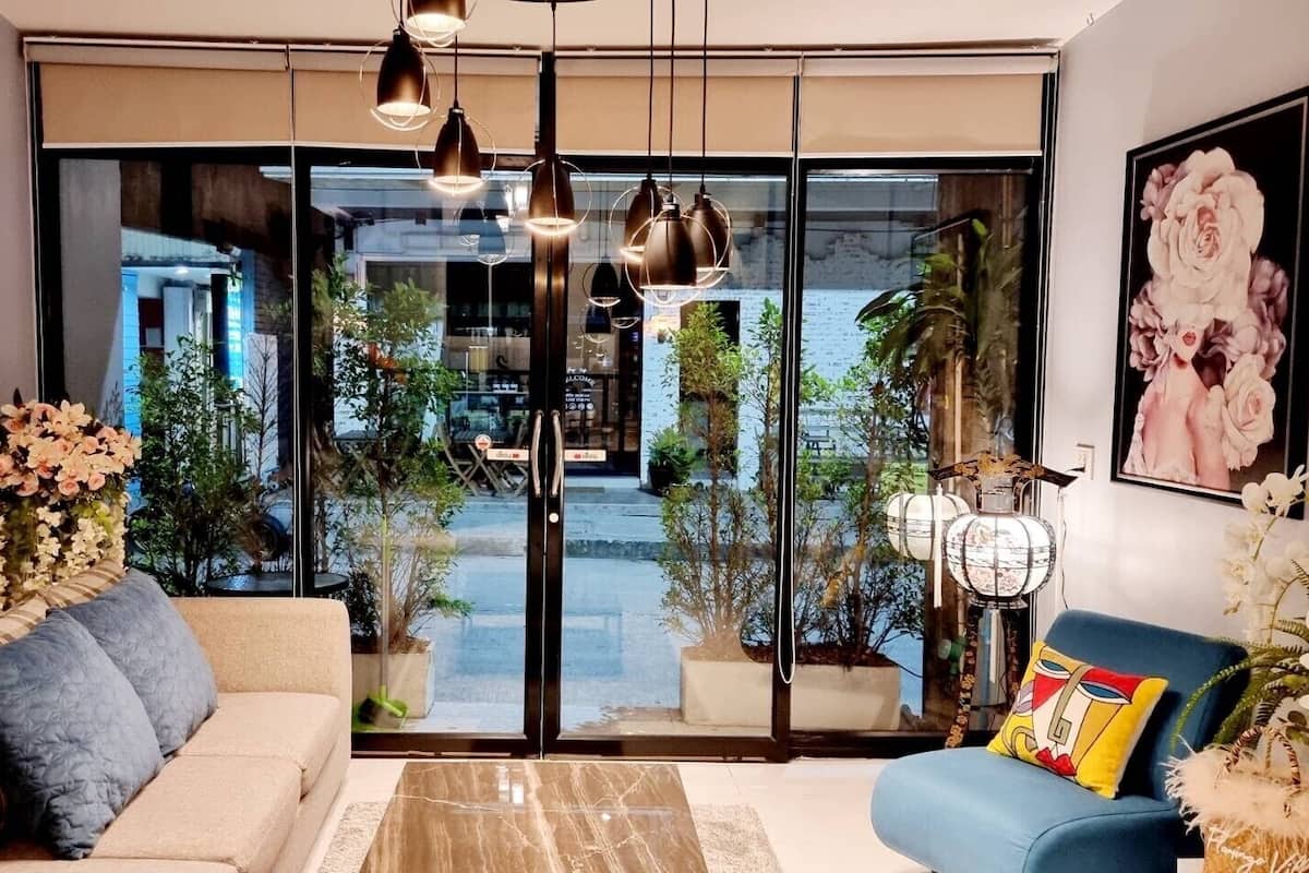 Ein modernes Wohnzimmer mit einer Couch, einem blauen Sessel und einer großen Glasdoor, die zu einem Außenbereich mit Pflanzen und Blick auf ein Gebäude führt.