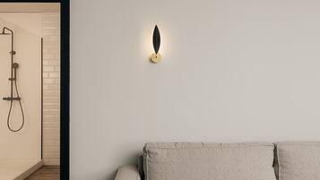 A modern interior with a beige sofa, a wall-mounted light fixture, and a shower area with a black frame.